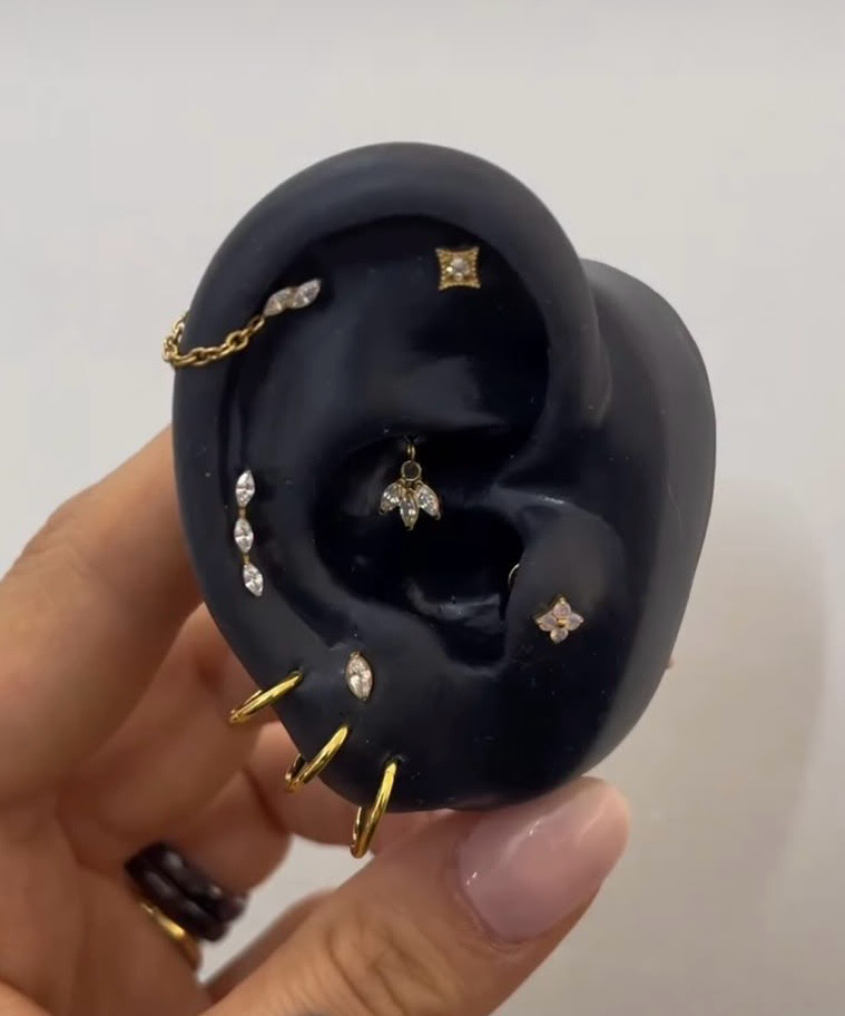 Composition originale de Margaux sur une oreille de présentation noire : anneaux dorés au lobe, pierres claires et chaîne sur le haut de l’oreille.
